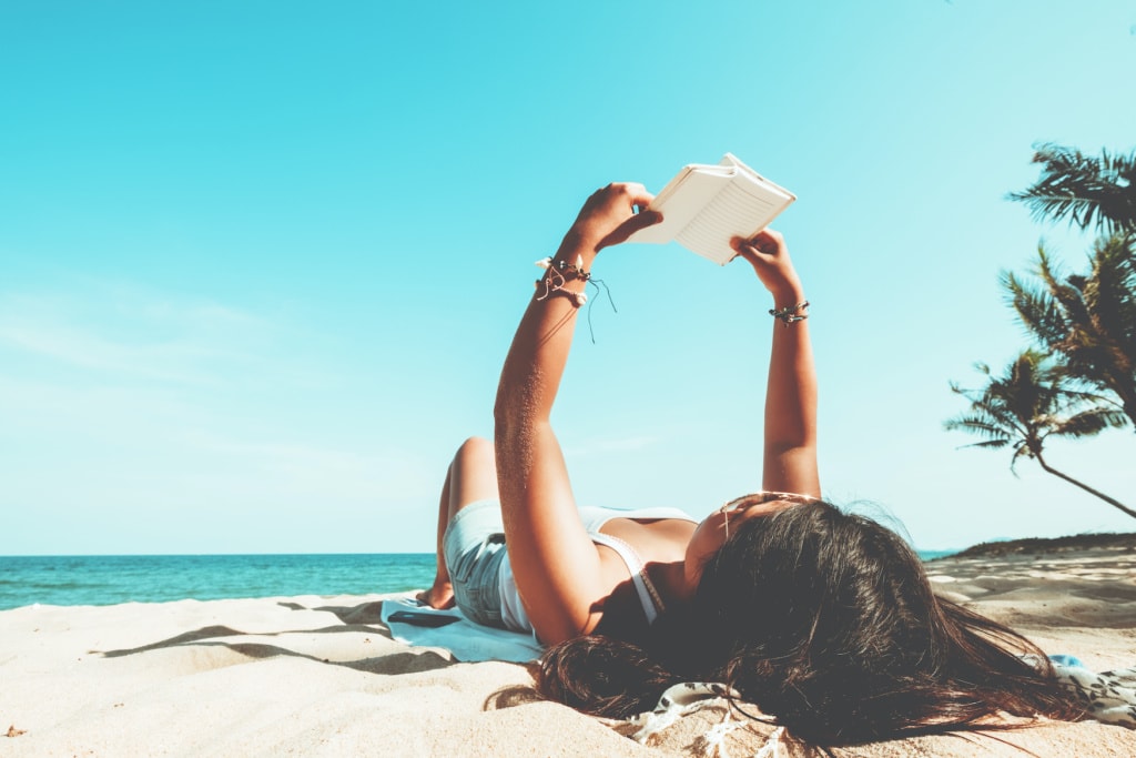 Mädchen liegt am Strand und liest ein Buch