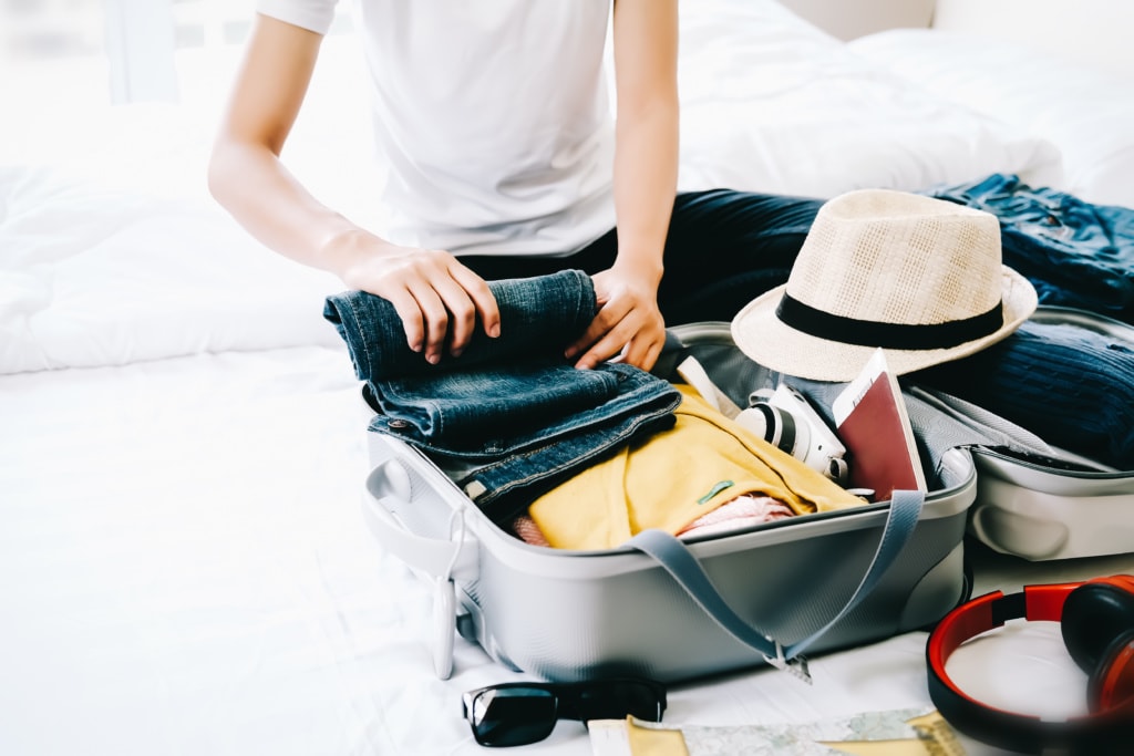 Mann rollt seine Jeanshose, um sie in seinen Koffer zu packen