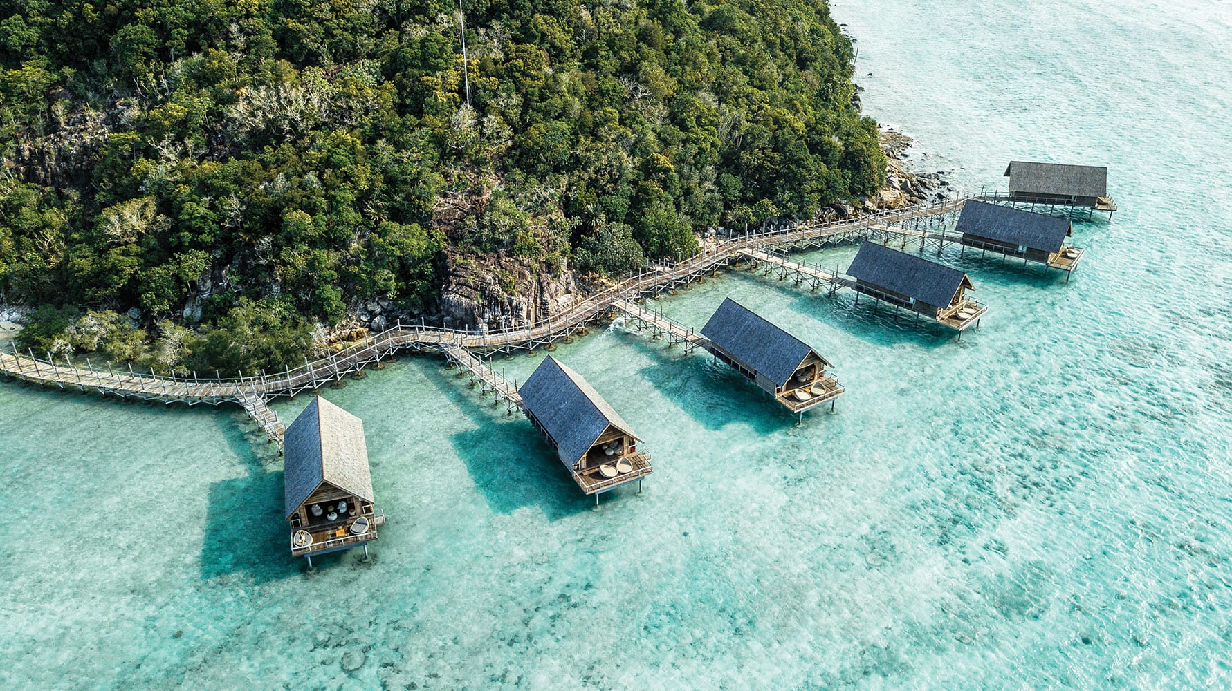 Sechs luxuriöse Villen liegen in türkisfarbenem Wasser vor einer indonesischen Insel
