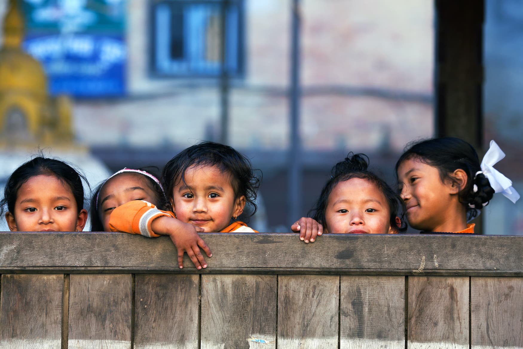 Mädchen in Schule in Nepal lächeln schüchtern in die Kamera und verstecken sich hinter Zaun