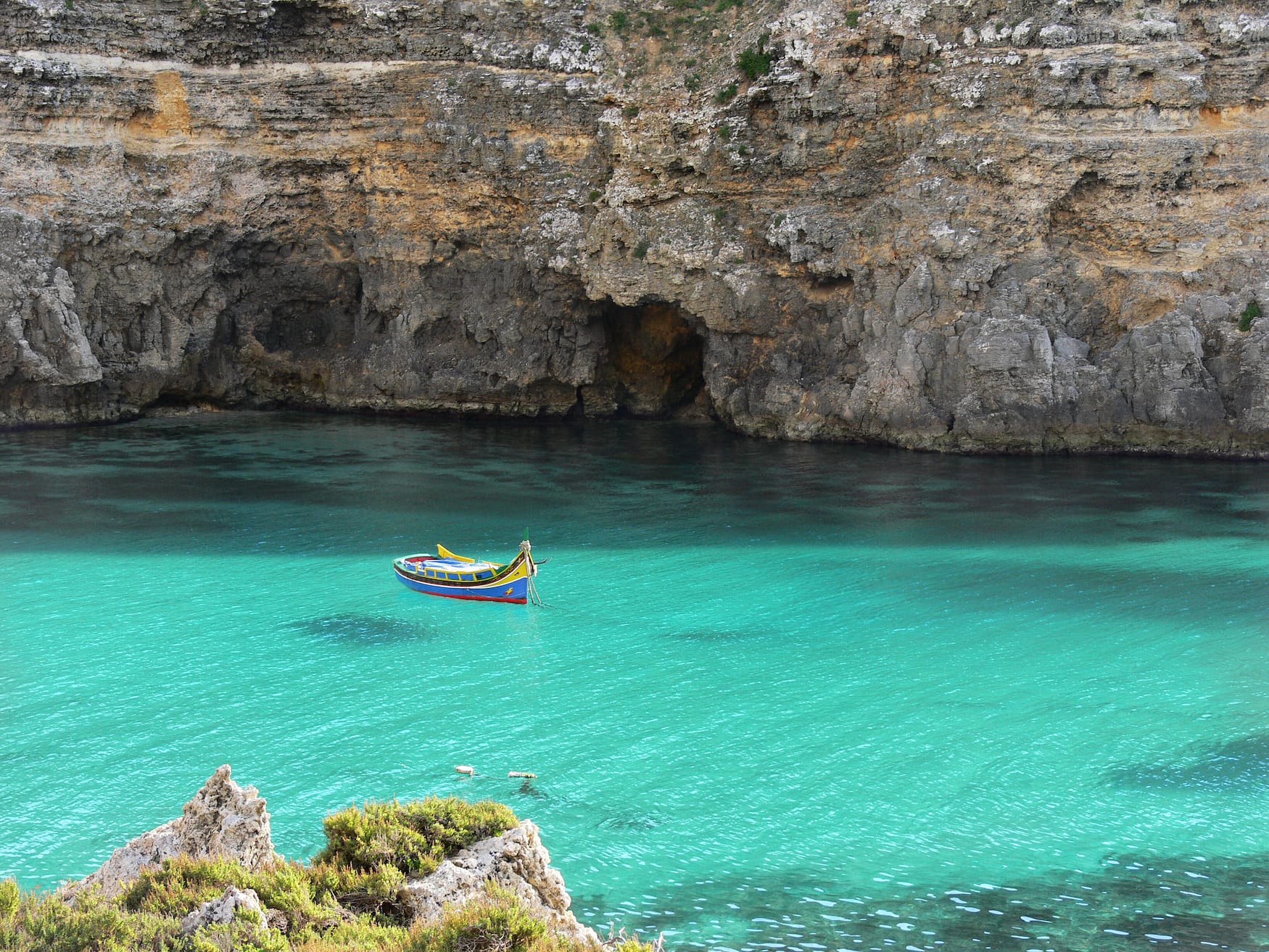 Buntes maltesisches Fischerboot "Iuzzu" schwimmt vor Anker im kristallklaren türkisfarbenen Wasser in einer Bucht der Insel Gozo
