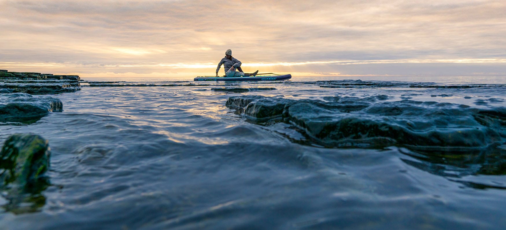 Mann sitzt auf einem SUP Board auf dem Meer