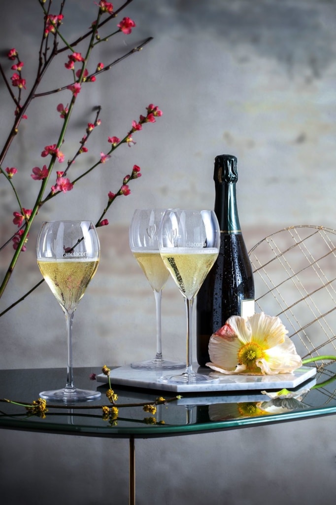 Glastisch mit Flasche Schaumwein und drei gefüllten Gläsern