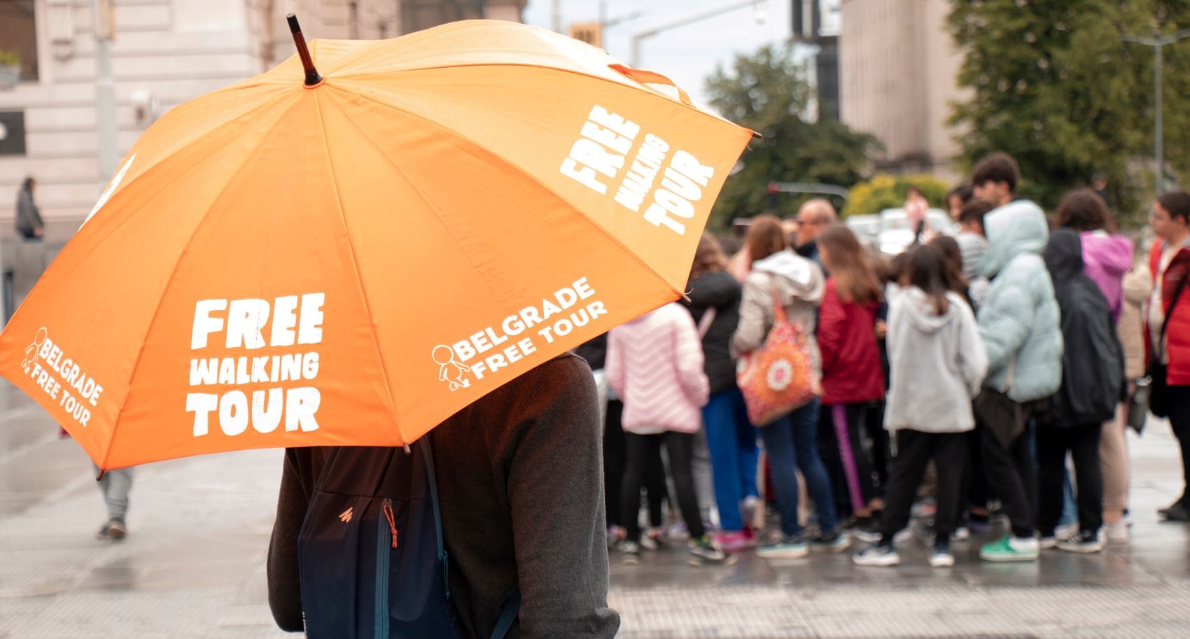 Reiseführer in Belgrad steht unter orangefarbenem Regenschirm mit der Aufschrift "Free Walking Tour" 