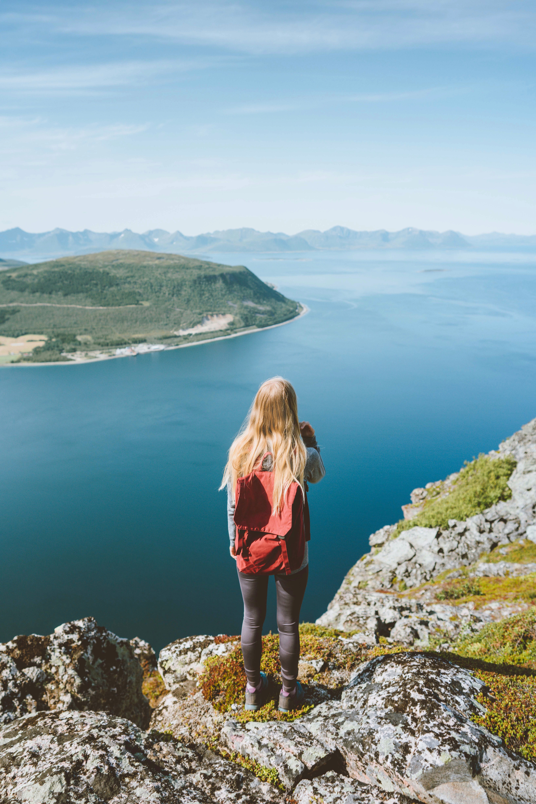Mädchen mit rotem Rucksack steht vor Fjorden in Norwegen