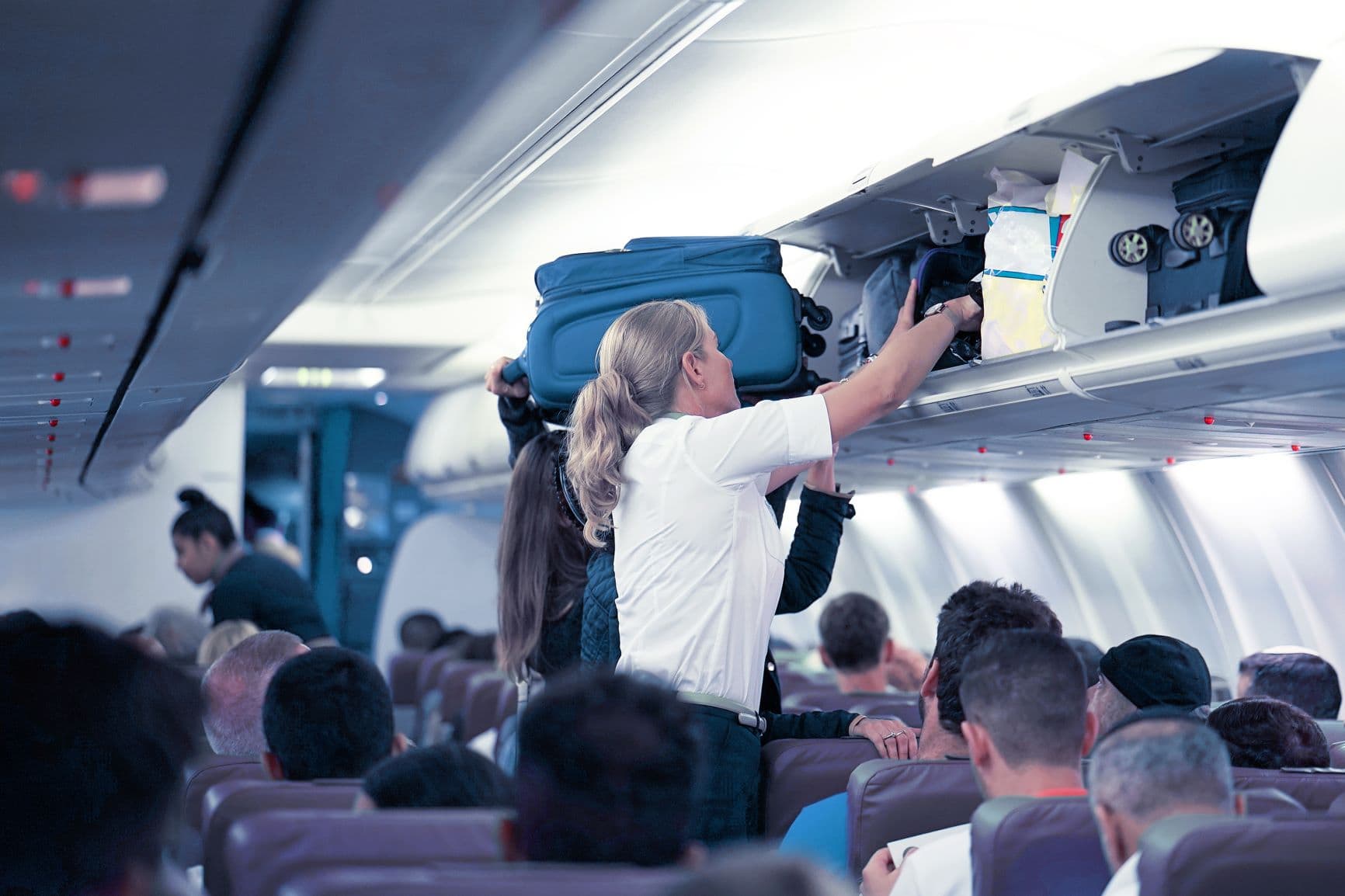 Flugbegleiterin hilft dabei, Koffer im Handgepäckfach zu verstauen