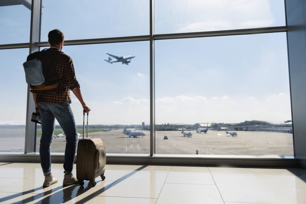 Mann steht im Flughafen mit Trolley und beobachtet Rollfeld