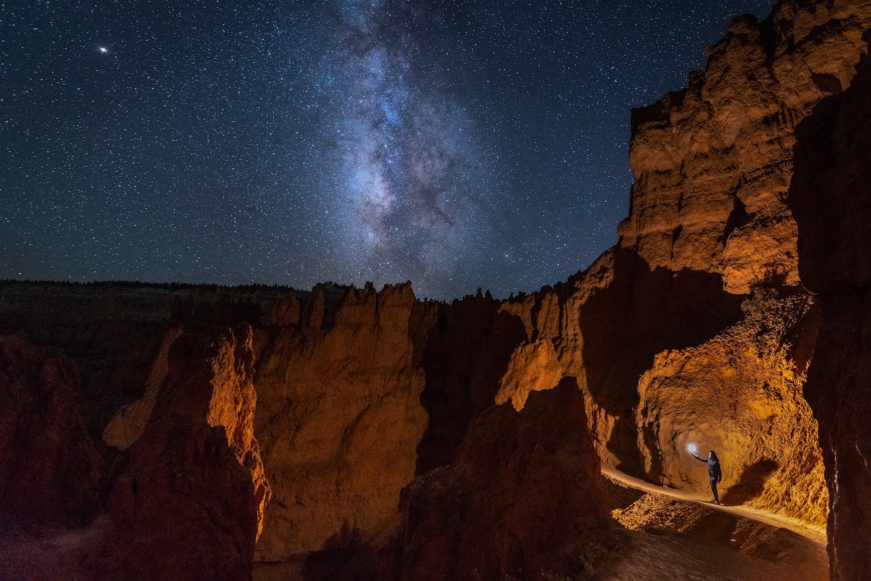 Mann mit Taschenlampe in Felsen von Bryce Canyon mit Milchstrasse