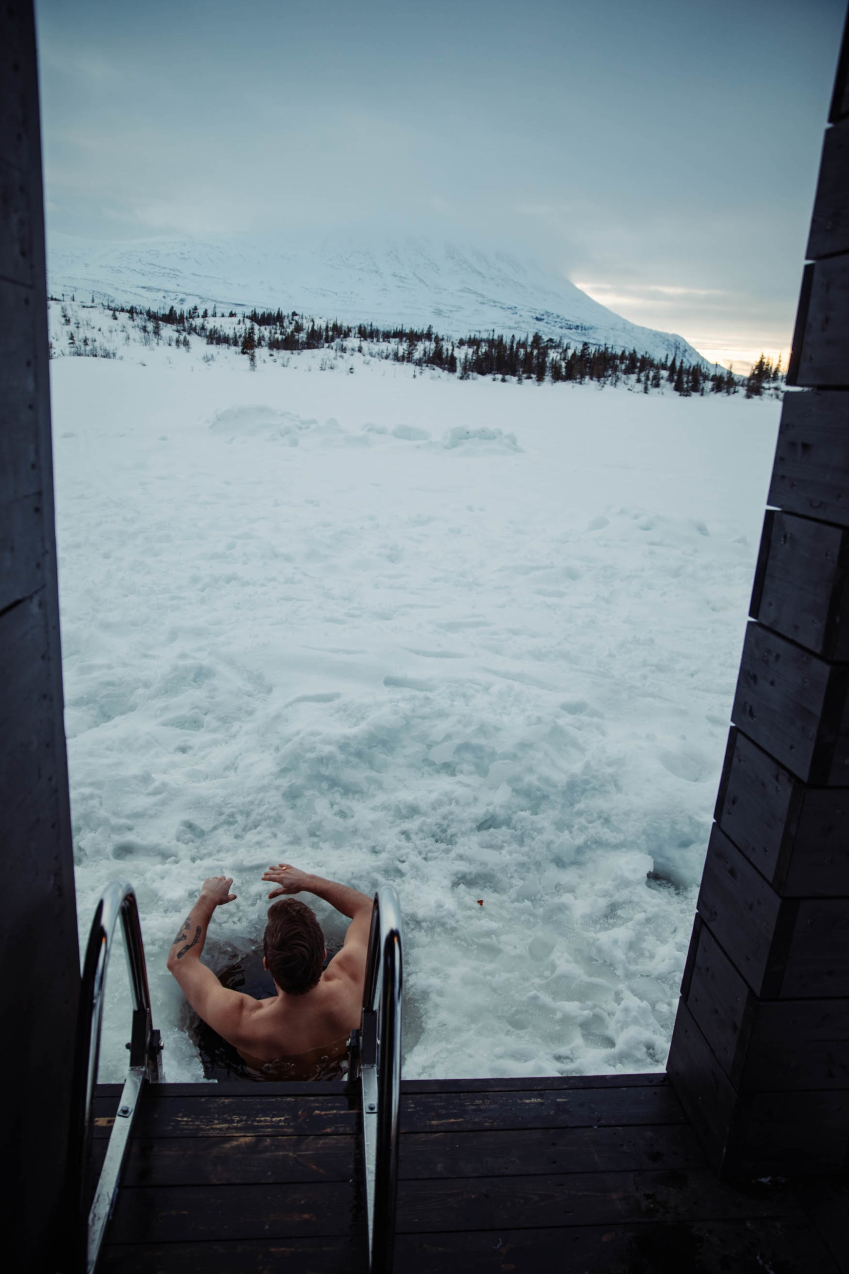 Mann nimmt ein Eisbad in verschneitem See nach Sauna