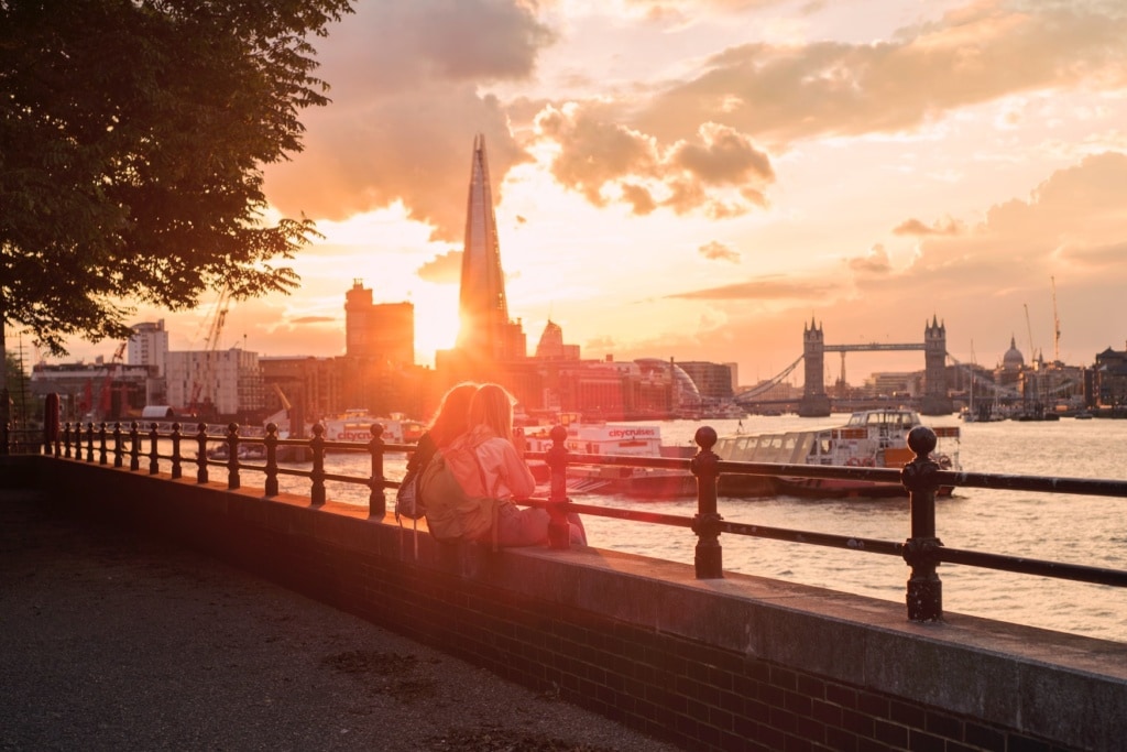 Zwei Freundinnen sitzen anders Themse in London bei Sonnenuntergang und freuen sich aufs Wochenende