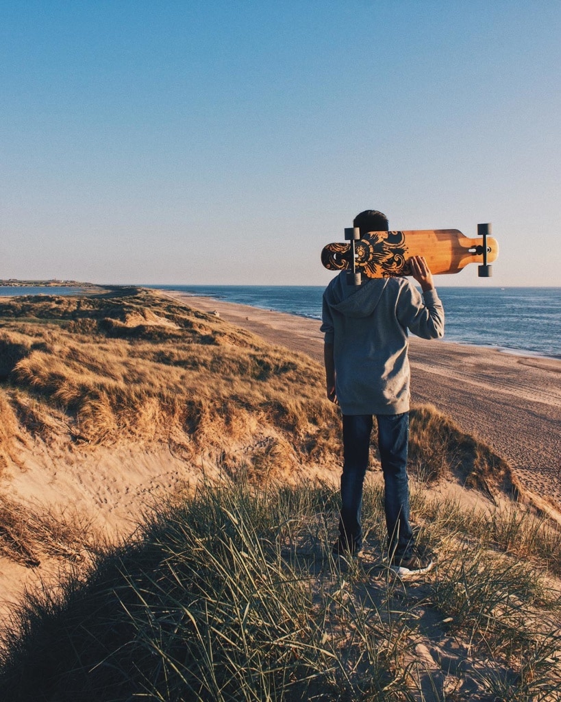 Mann mit Skateboard am Strand von Dänemark