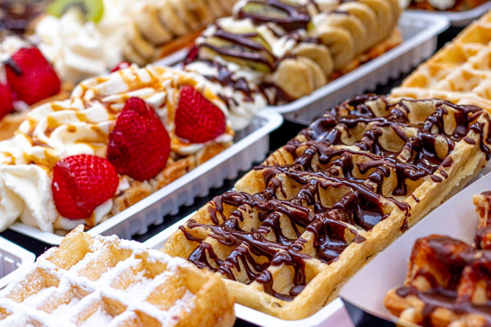 Waffel-Auswahl in einer Auslage, teils überzogen mit Schokolade, teils mit Erdbeeren oder Bananen 