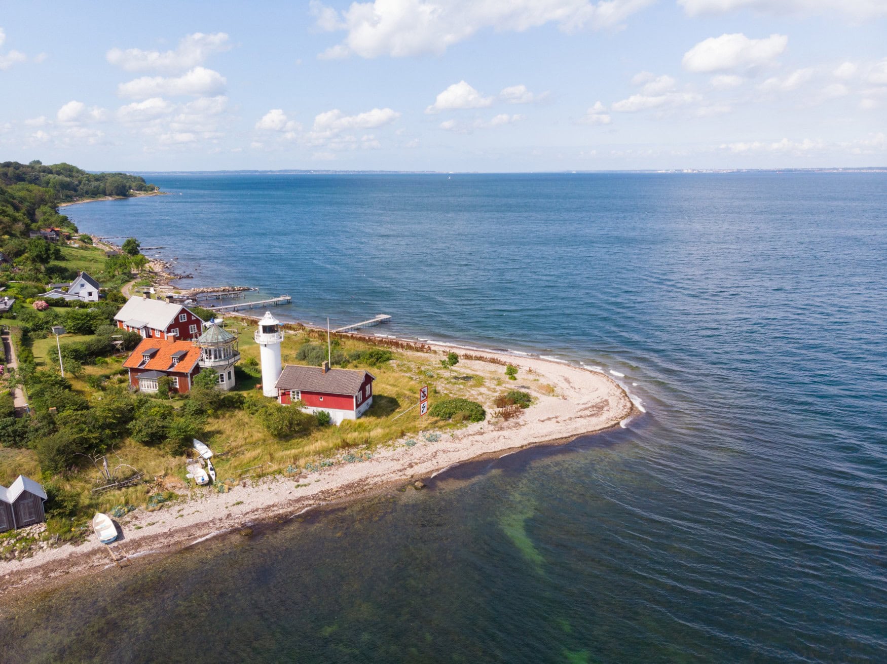 Die Landspitze einer Insel ragt ins Meer, darauf einige Häuser und ein weißer Leuchtturm. Mit der Drohne aufgenommen.