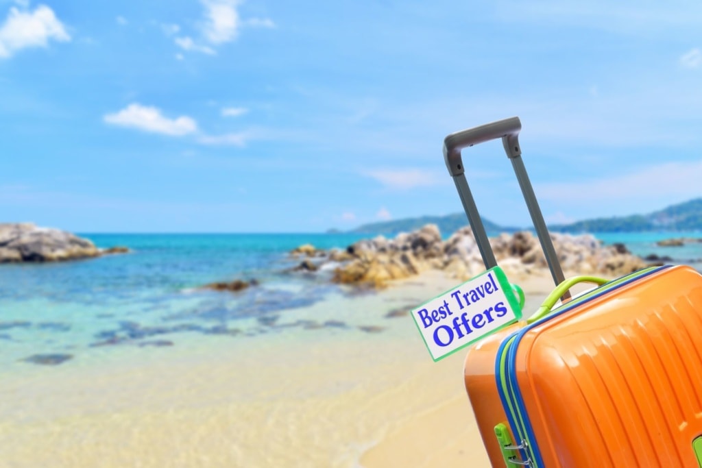 Koffer mit Aufschrift "Best Travel Offer" am Strand