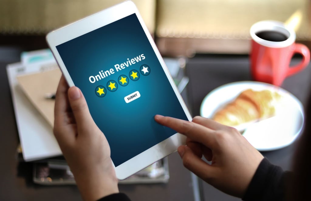 Person hält Tablett in der Hand, auf dessen Display "Online Reviews" steht