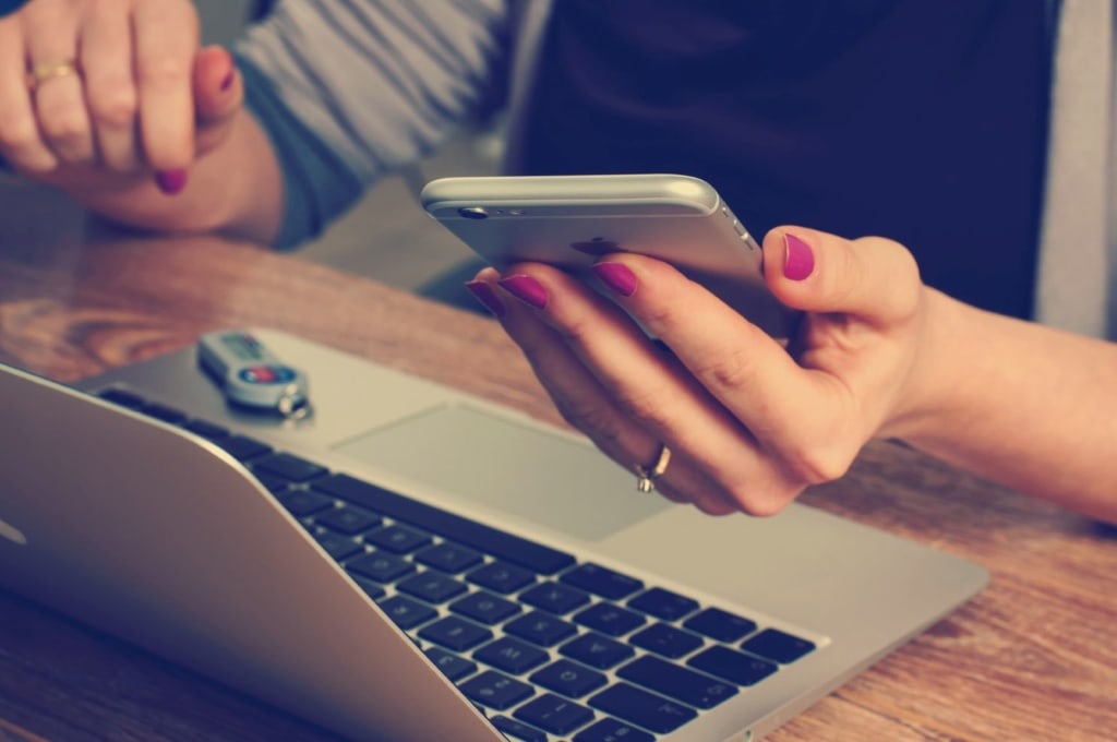 Frau sitzt vor Notebook und hält Apple-Handy in der Hand