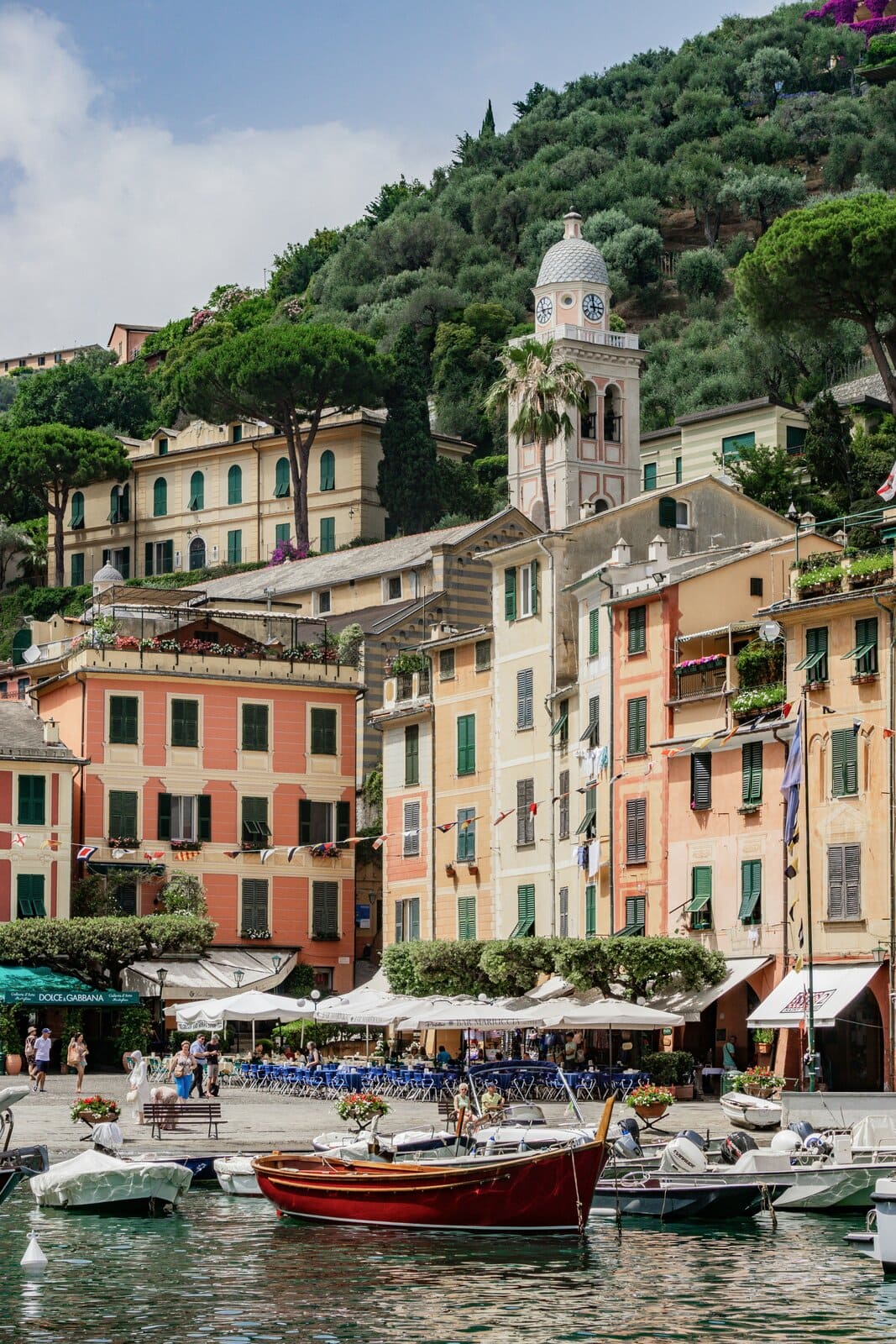 Piazzetta von Portofino mit pastellfarbenen Fassaden, dem Glockenturm der Kirche San Martino und einem roten Holzboot im Vordergrund.