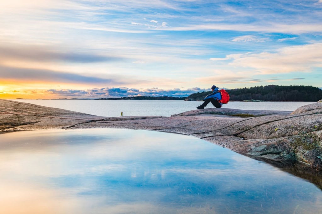 Natururlaub in Schweden: Mann sitzt an Küste auf Felsen und genießt die Aussicht