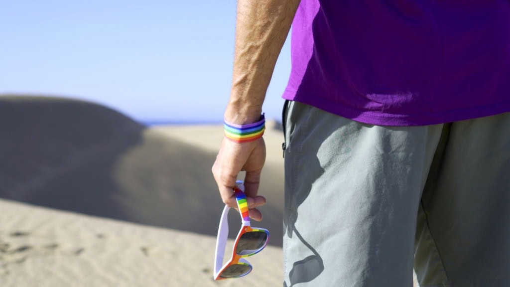 Mann in den Dünen in Maspalomas auf Gran Canaria mit Regenbogen-Accessoires