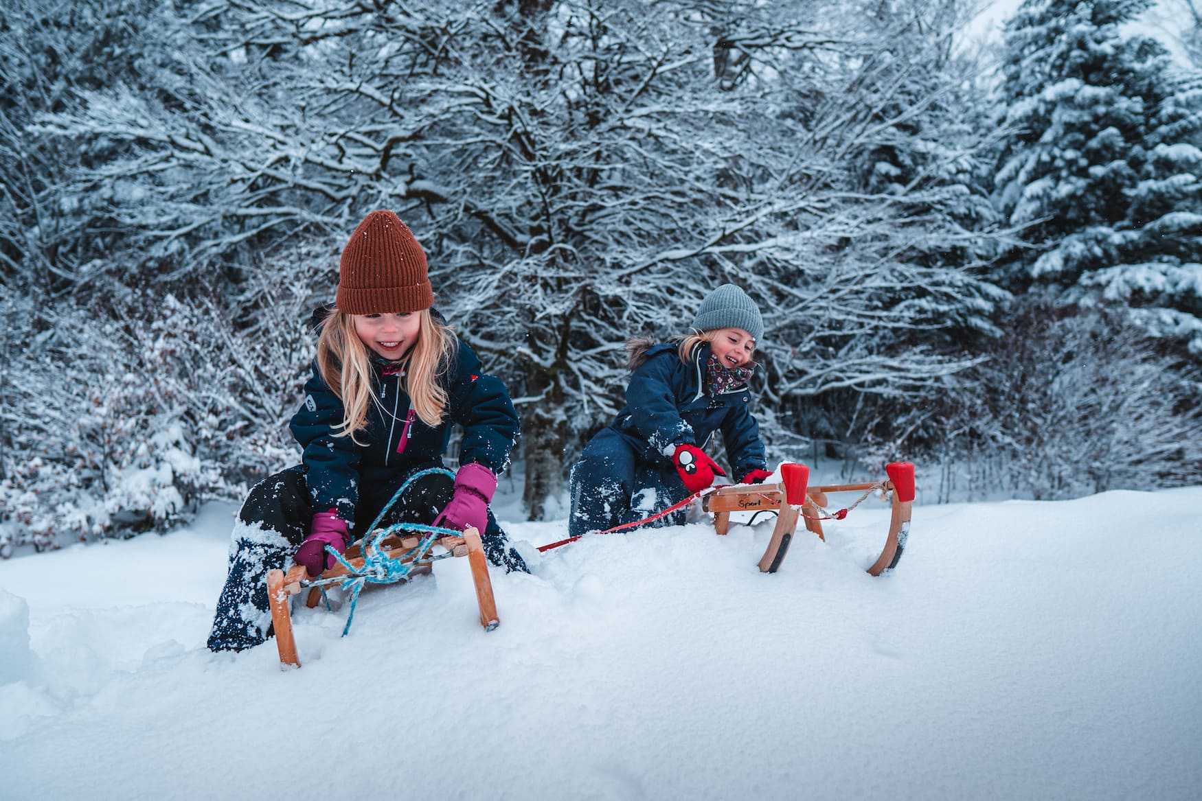 Zwei rodelnde Kinder in verschneitem Wald