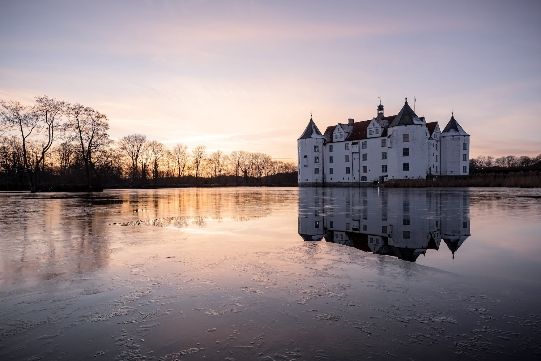 Das historische Wasserschloss in Glücksburg im Licht der untergehenden Wintersonne. Auf dem Schlossteich bildet sich eine Eisfläche