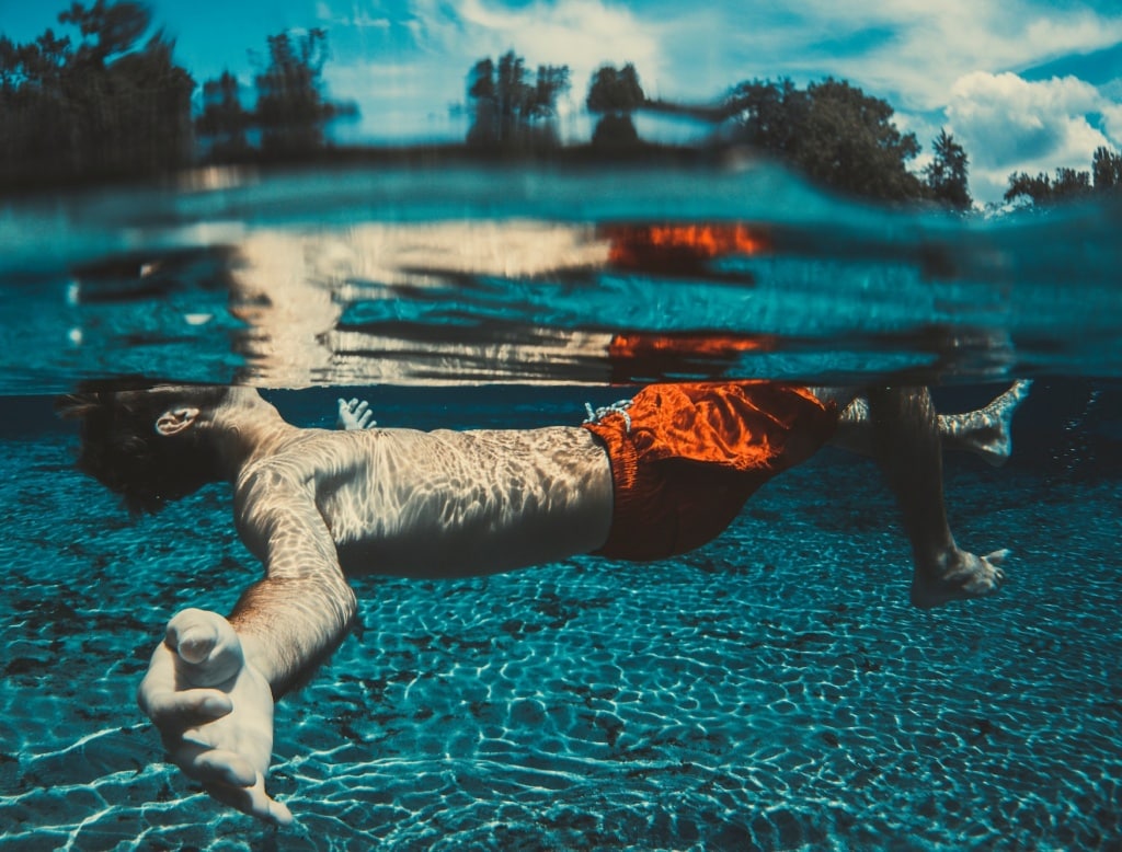 Mann in roter Badeshorts schwimmt in Pool