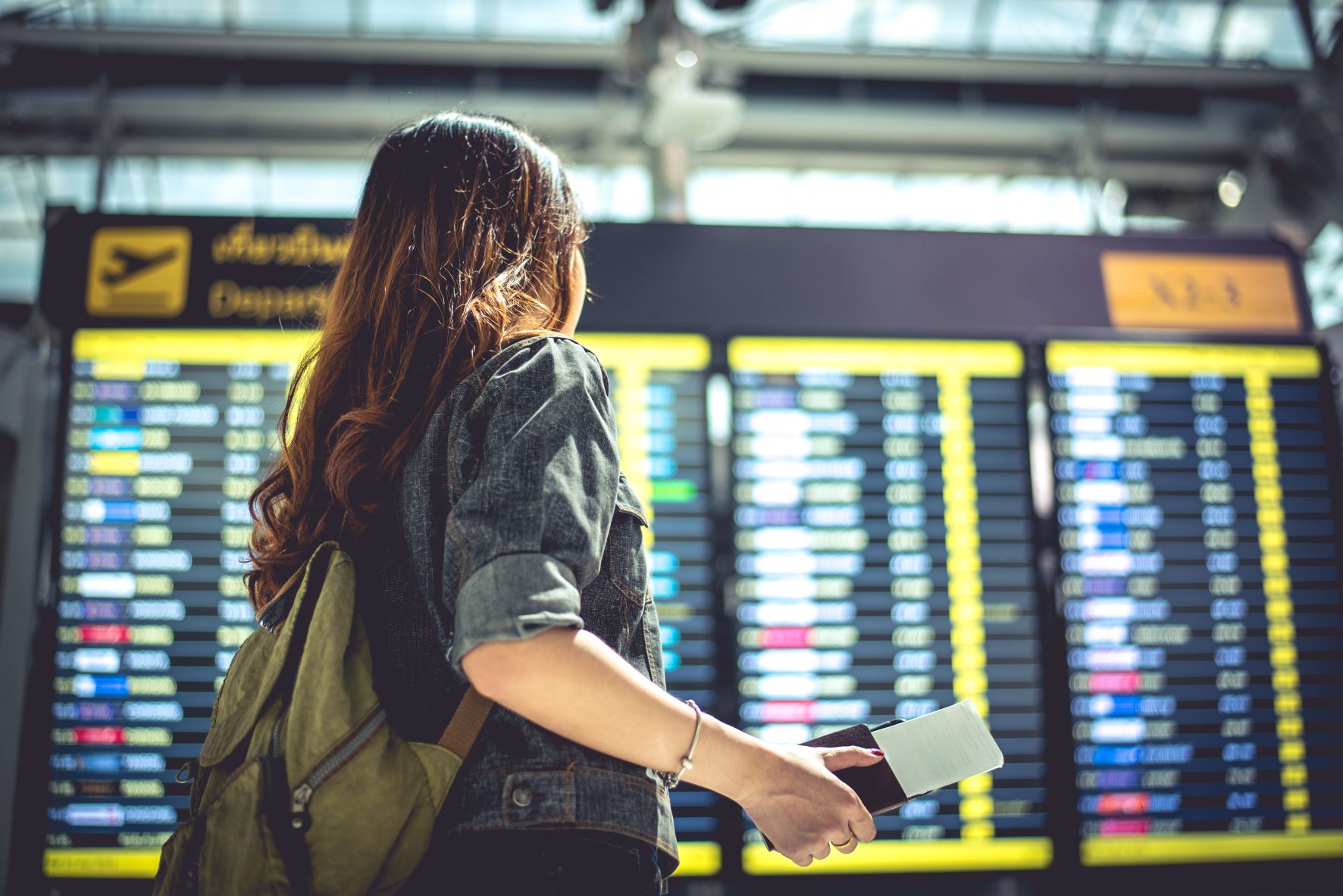 Frau blickt am Flughafen auf die Abflug-Anzeigetafel 