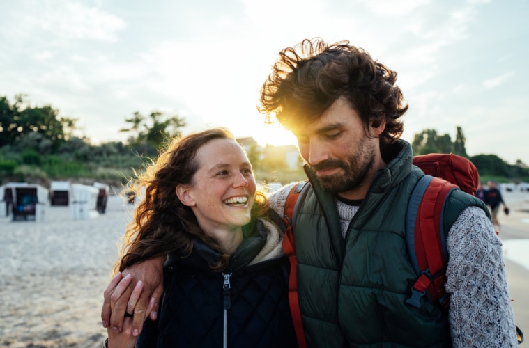 Ein Par spaziert am Strand vom Ostseebad Heringsdorf in den Sonnenuntergang nach einem Wandertag. | TMV/Gänsicke