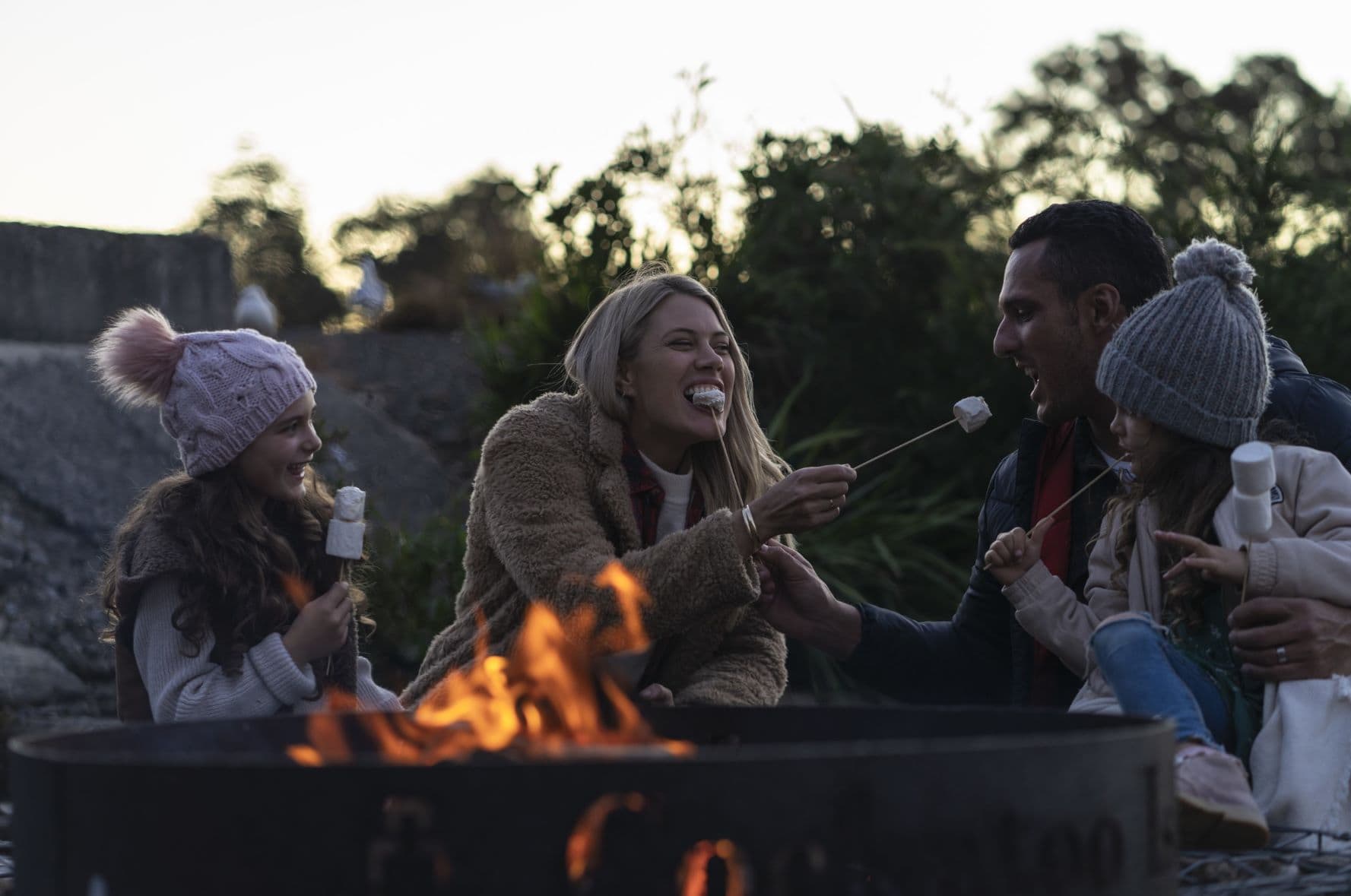 Familie sitzt an einem offenen Grill im Freien und isst Marshmallows 