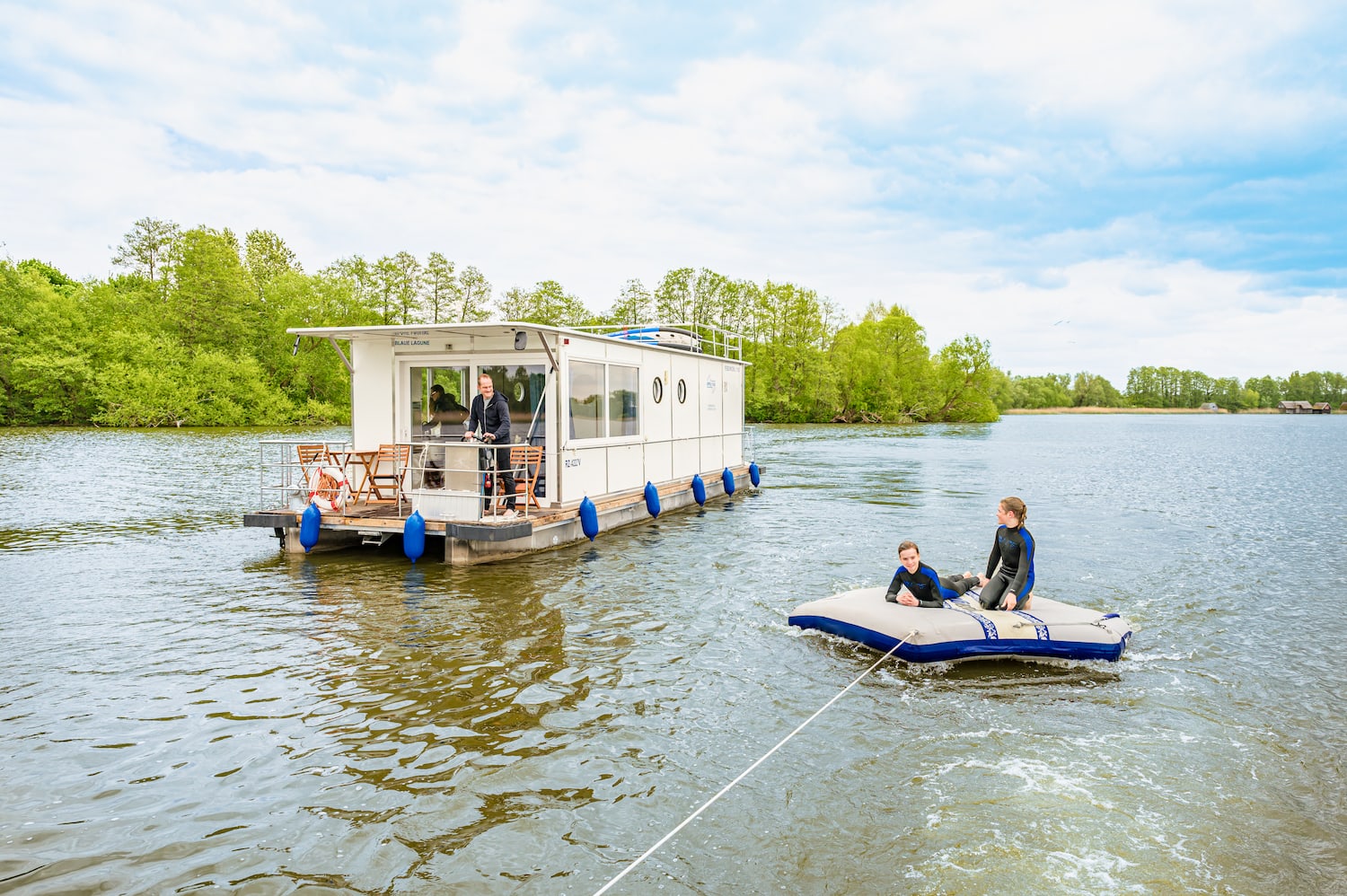 Kinder treiben auf einer Luftmatratze hinter dem Hausboot her.