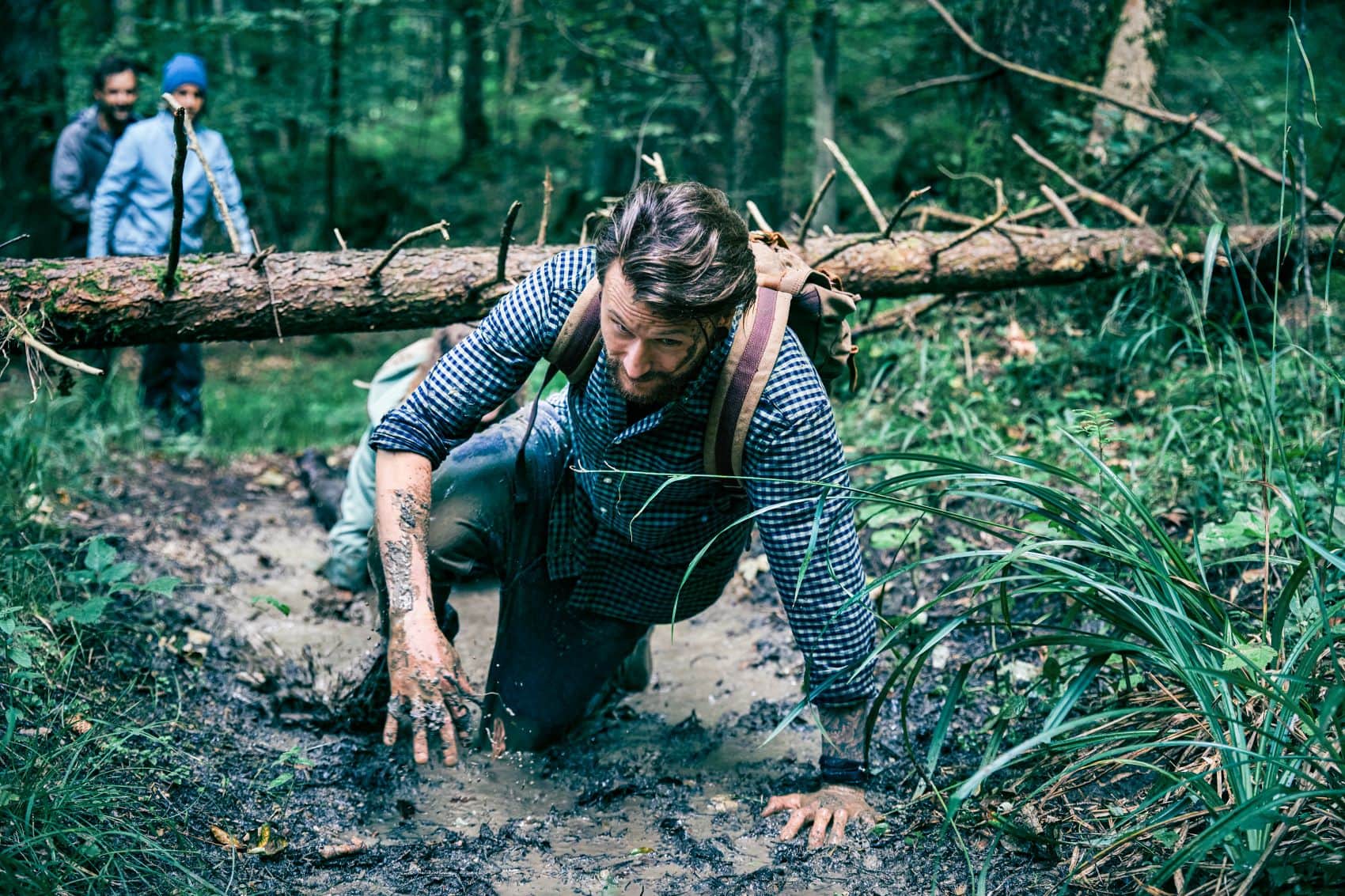 Mann robbt sich unter Baumstamm im Wald