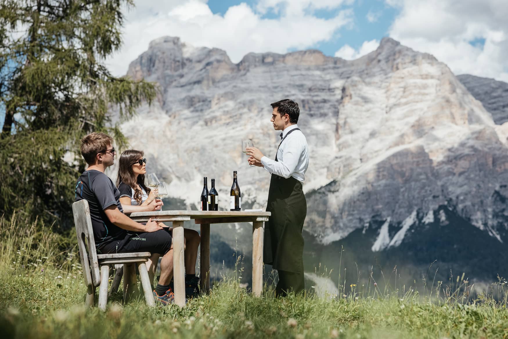 Weinverkostung Vins alaleria in Alta Badia: Ein Paar sitzt draußen an einem Tisch und wird vom Sommelier beraten 