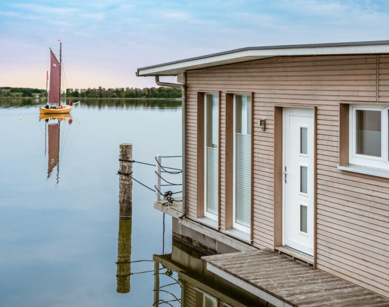 Schwimmendes Haus im Naturhafen Krummin mit einem Zeesboot im Hintergrund