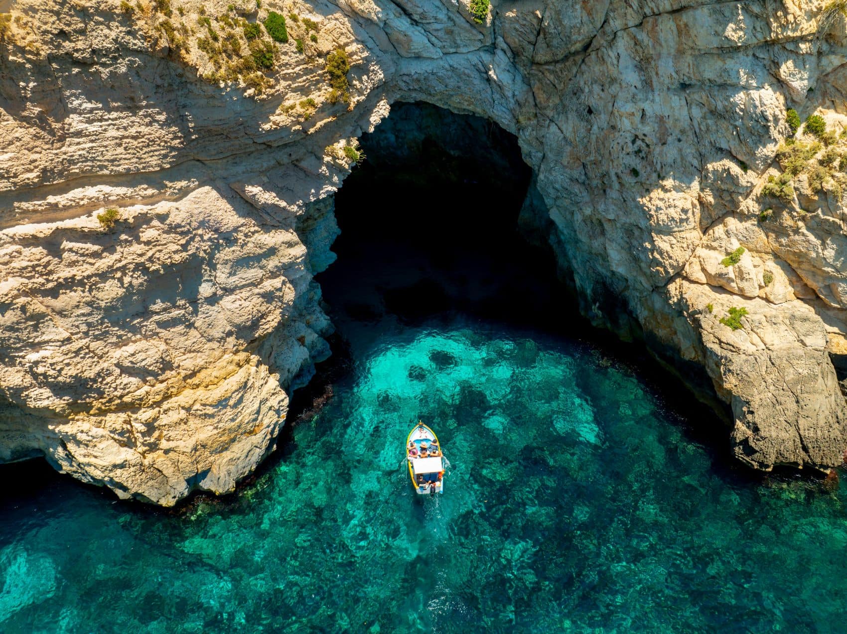 Drohnenaufnahme eines Bootes, das in die Blaue Grotte auf Malta hineinfährt 