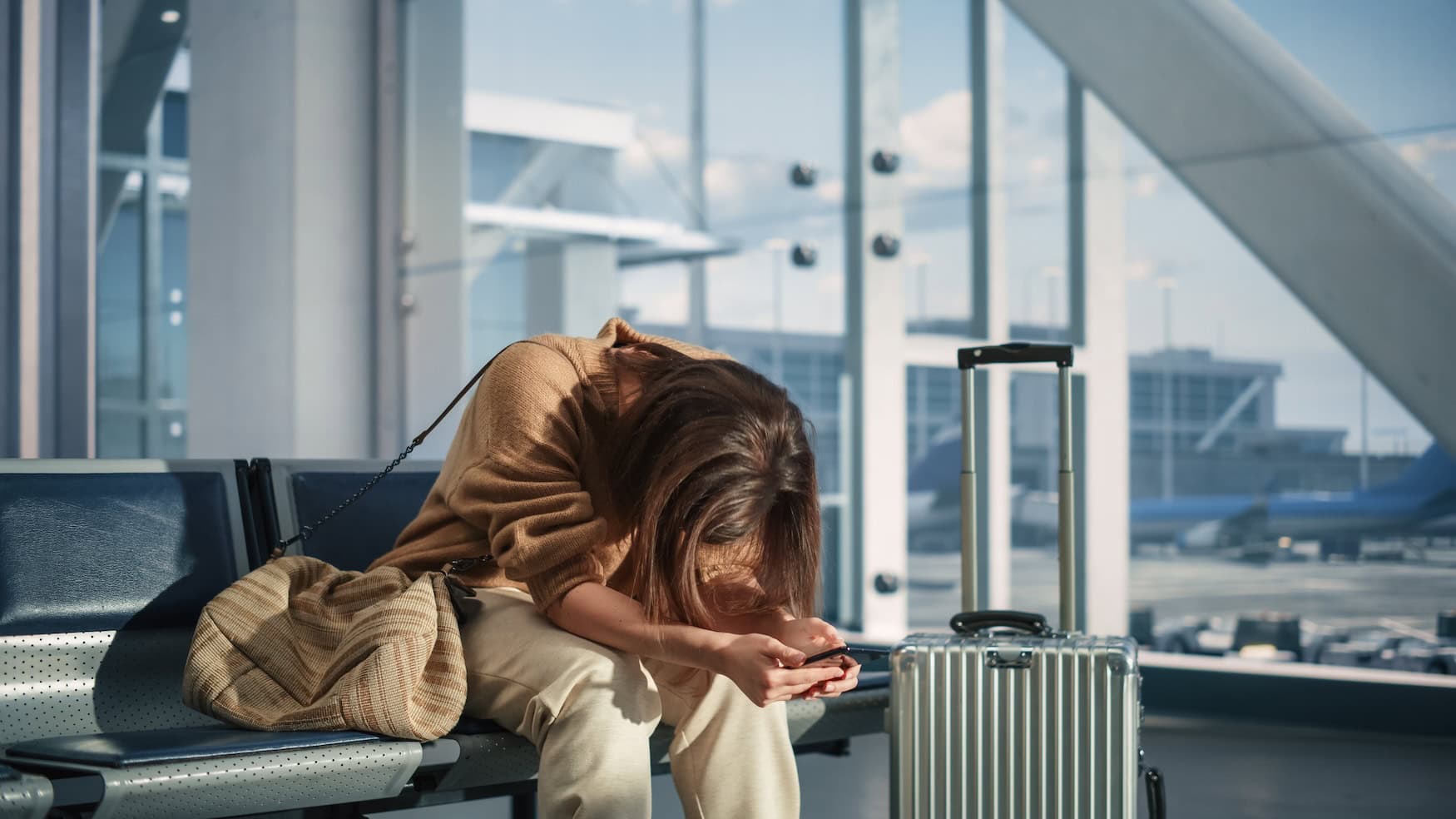 Anschlussflug verpasst: Eine Frau sitzt traurig am Flughafen.