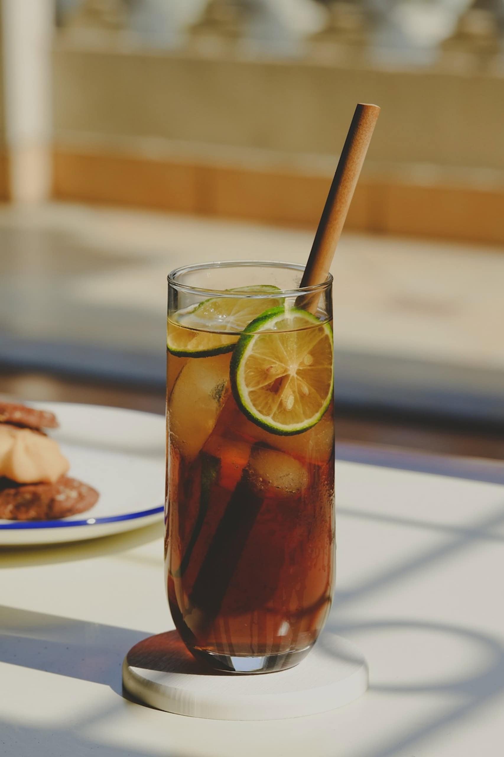 Ein hohes Glas mit Eistee, darin einige Schnitzer Limette und Pfirsich sowie ein Strohhalm aus Pappe