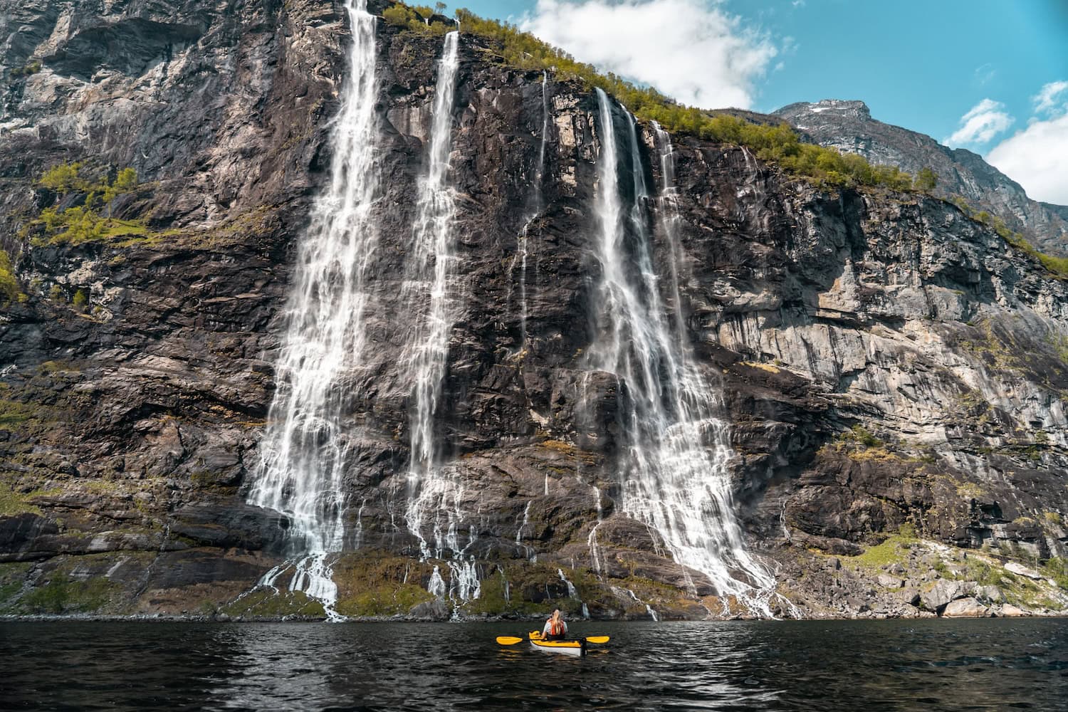 Eine Frau sitzt in einem Paddelboot vor dem Seven Sisters Wasserfall in Norwegen
