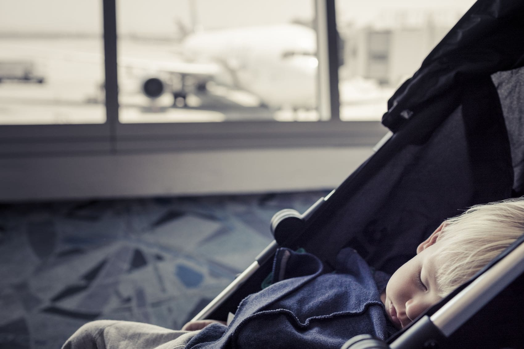 Kleiner Junge schläft im Flughafen in einem Kinderwagen