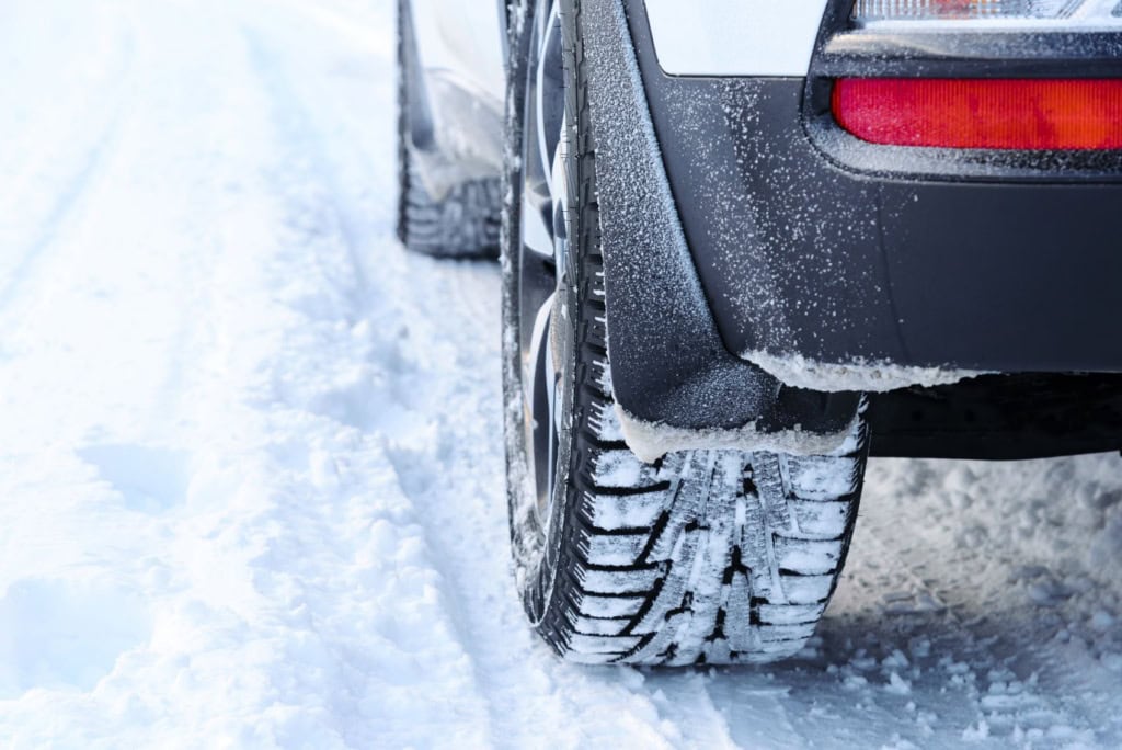 Nahaufnahme Winterreifen an Auto auf verschneiter Straße