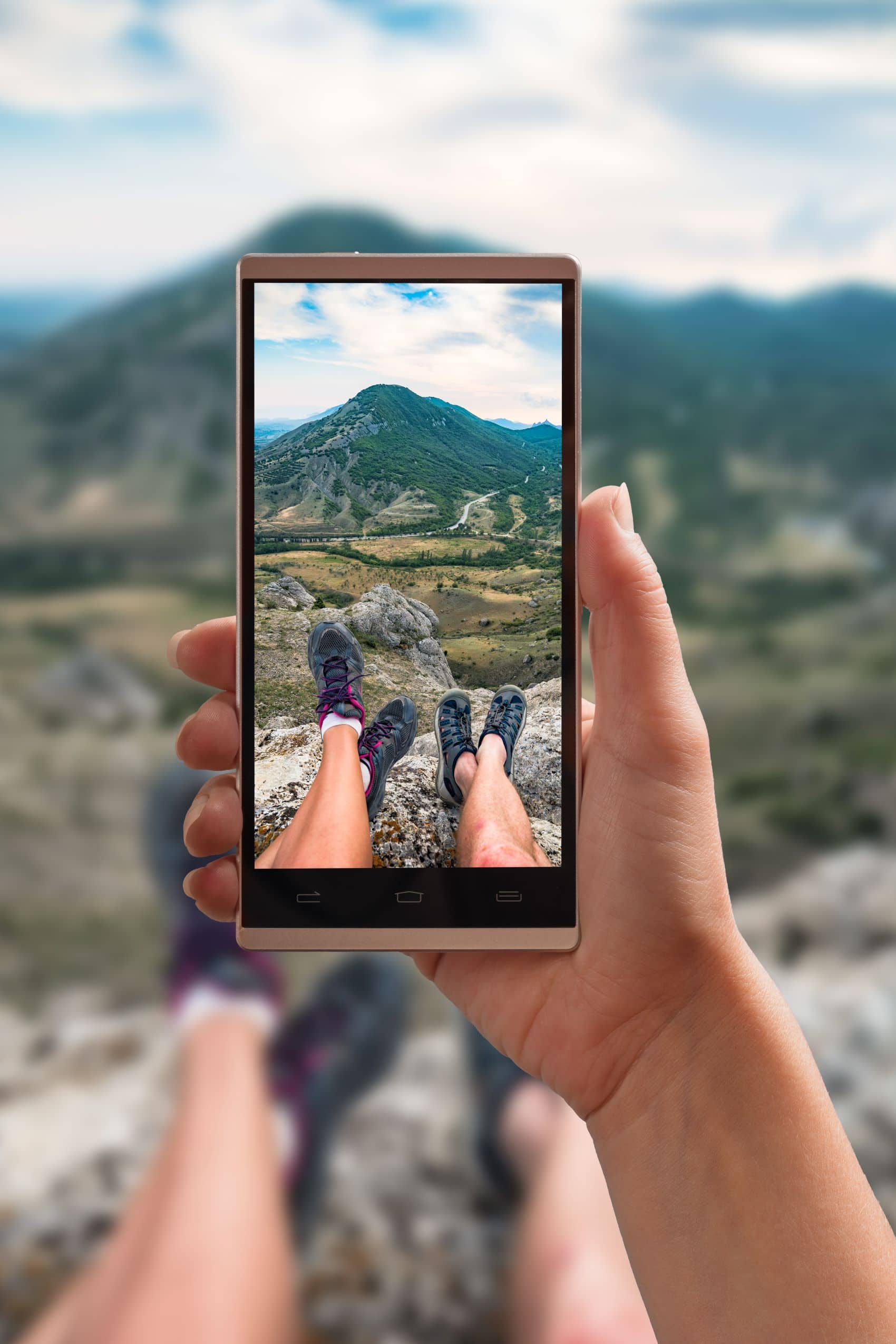 Nahaufnahme eines Handy-Displays. Bild zeigt Beine von Wanderern und Berg im Hintergrund