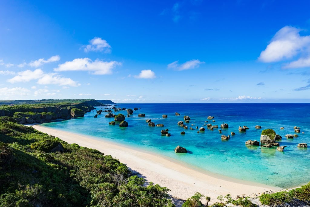 An einem tropischen Strand in Okinawa, Japan, ragen mehrere kleine Felsen aus dem Meer in einer Bucht.