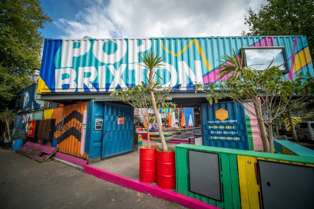 Mehrere bunt bemalte Schiffscontainer sind zu einer Art Tor aufgestapelt. Auf dem obersten ist in großer Schrift "Pop Brixton" zu lesen.