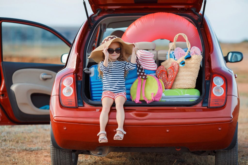 Bild zu Mietwagen buchen bei Sunny Cars: Ein Mädchen sitzt im Kofferraum eines Mitautos.