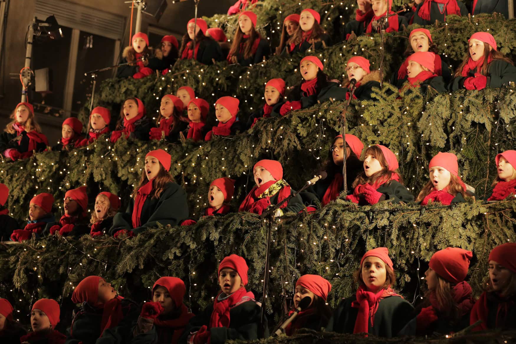 Kinder mit roten Mützen auf dem Kopf singen im Chor.