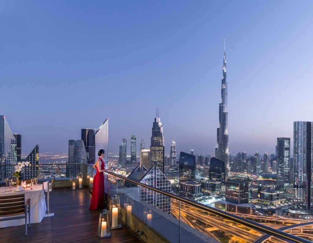 Eine Frau in rotem Abendkleid blickt von der Dachterrasse des Shangri-La Dubai auf die Dämmerung über der Skyline von Dubai