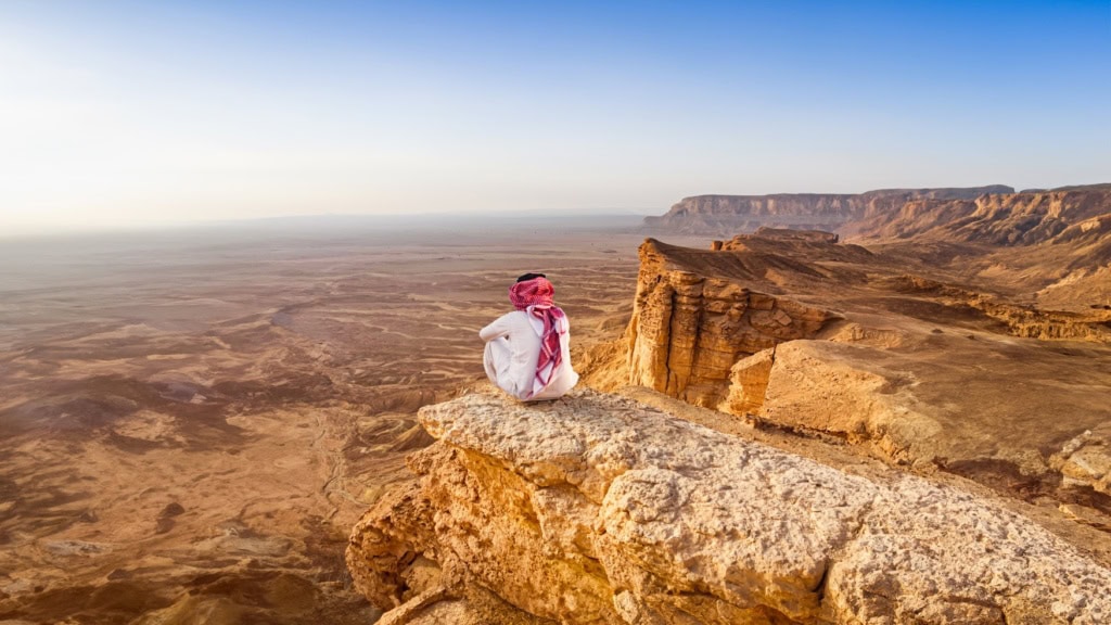 Ein Mann sitzt auf einem Berg und blickt in die Wüste.