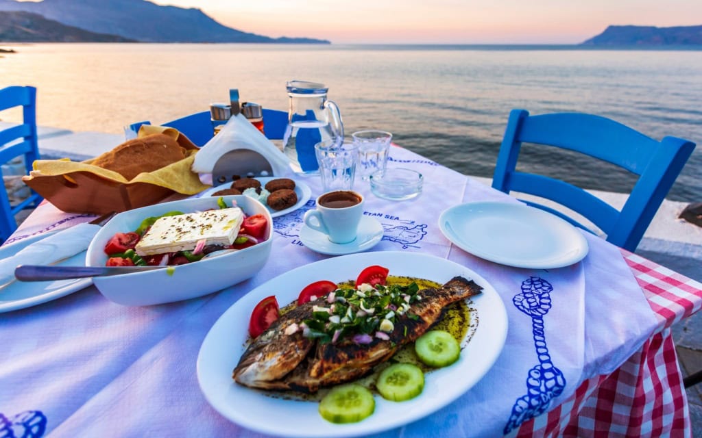 Fisch und griechischer Salat auf einem Tisch am Meer in Kreta, Griechenland.