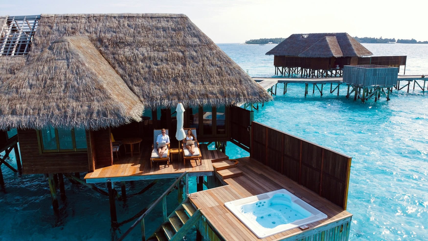 Zwei Personen sitzen mit Laptop auf dem Schoß auf der Terrasse einer Overwater-Villa.