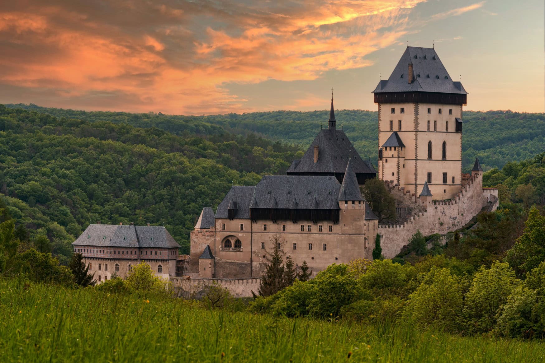 Auf einer Waldanhöhe steht eine gut erhaltene Burg, mittig ein Wohngebäude und rechts ein mächtiger Bergfried. Dahinter Wald bis zum Horizont, der in das rote Licht der Abendsonne getaucht ist.