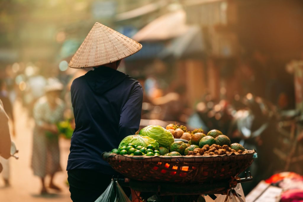 Eine Frau führt in Vietnam mit einem beladenen Fahrrad durch eine Straße.